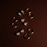 Gold hoop earrings with removable emerald, heart, and pear diamond drops on a dark red background