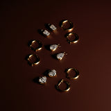 Gold hoop earrings with removable emerald, heart, and pear diamond drops on a dark red background