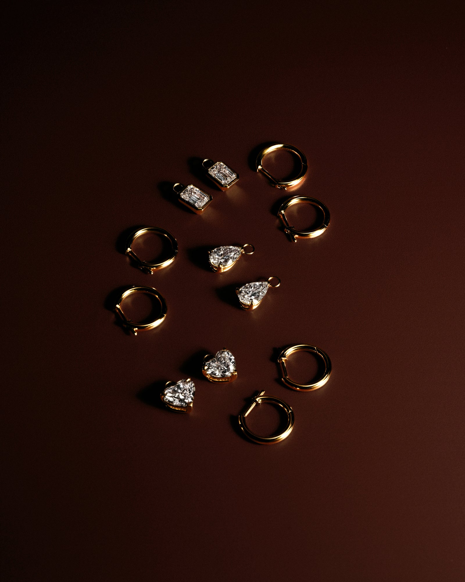 Gold hoop earrings with removable emerald, heart, and pear diamond drops on a dark red background