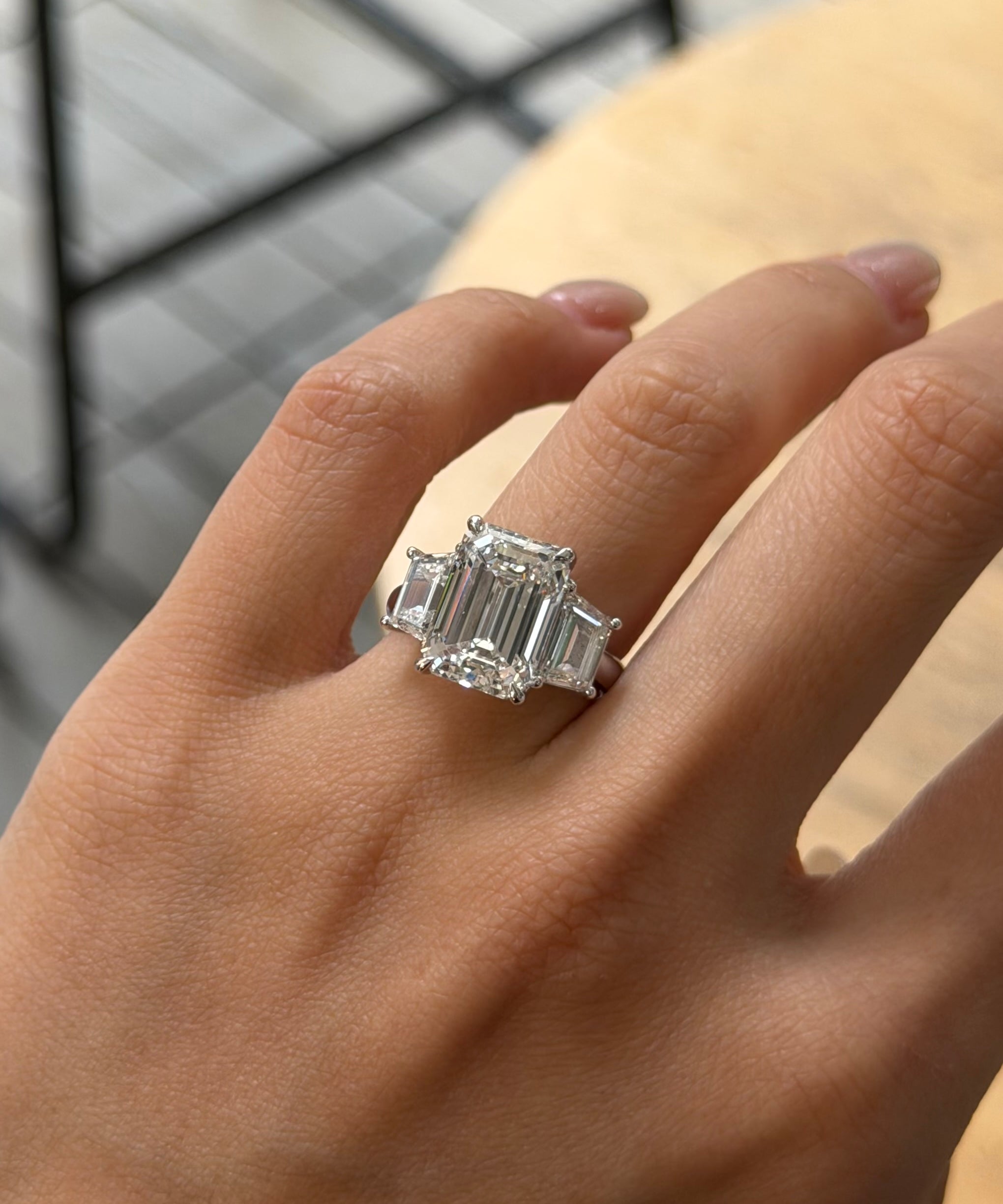 Hand wearing a diamond engagement ring with a 5ct emerald cut diamond center stone and trapezoid cut diamonds.