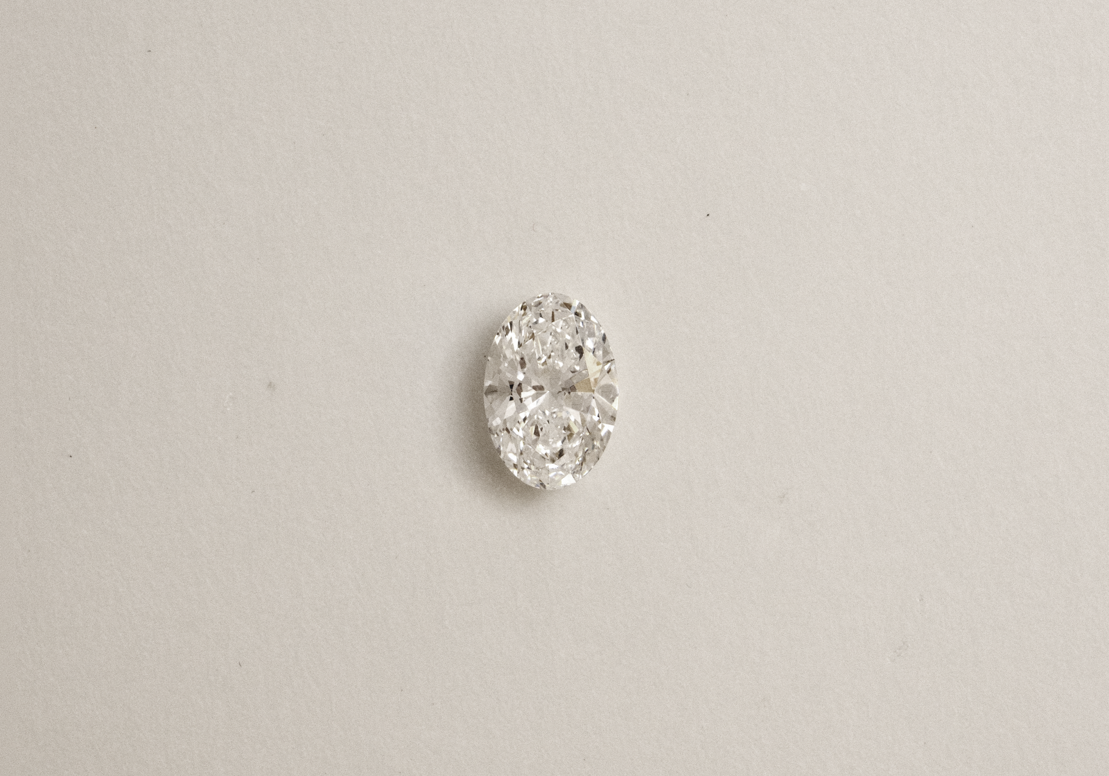 A single oval cut diamond on a light beige background