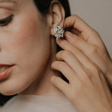 Close-up of audrey pecot wearing a tinxx asscher diamond earring with a hand adjusting it.
