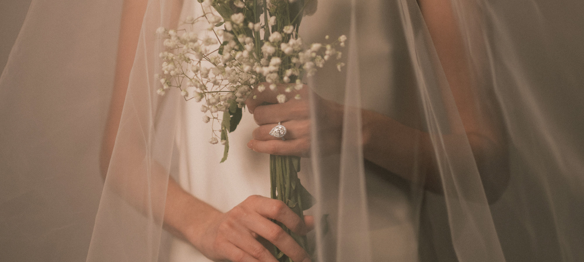 Bride holding a bouquet of flowers and wearing a tinxx pear cut diamond halo ring with a soft veil