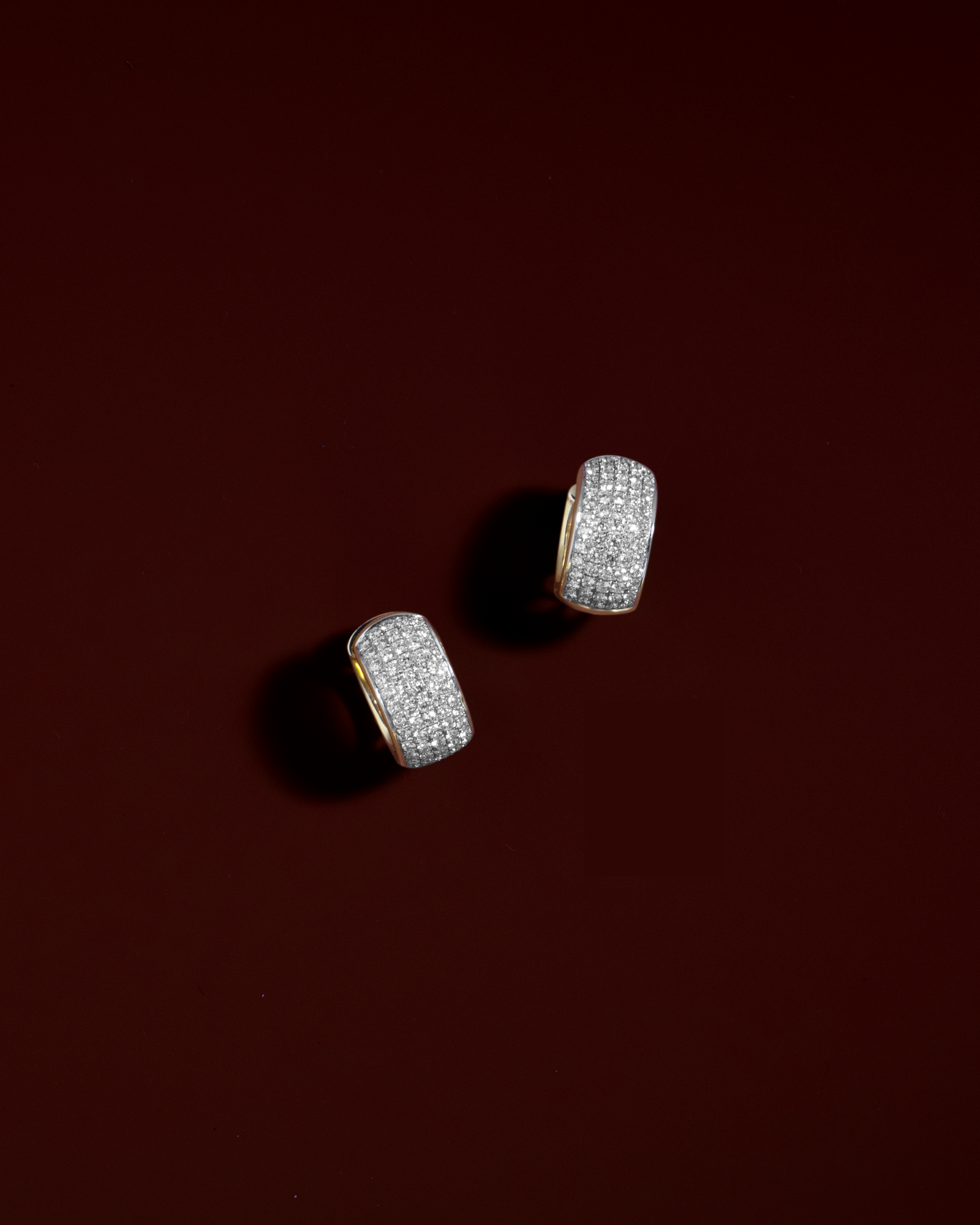 diamond huggie earrings in 18K yellow gold against red background