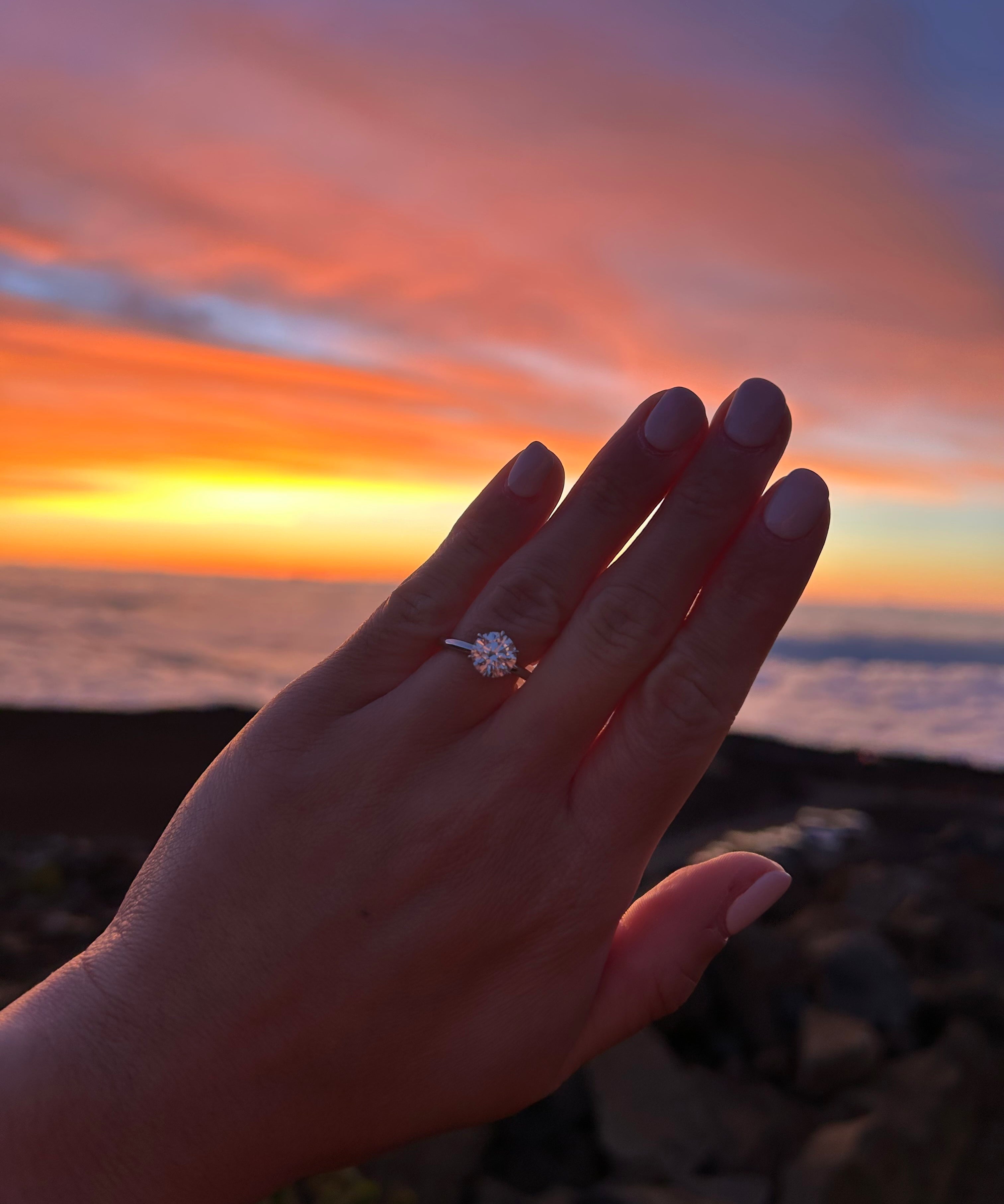 Hand wearing a tinxx ring with a sunset in Hawaii