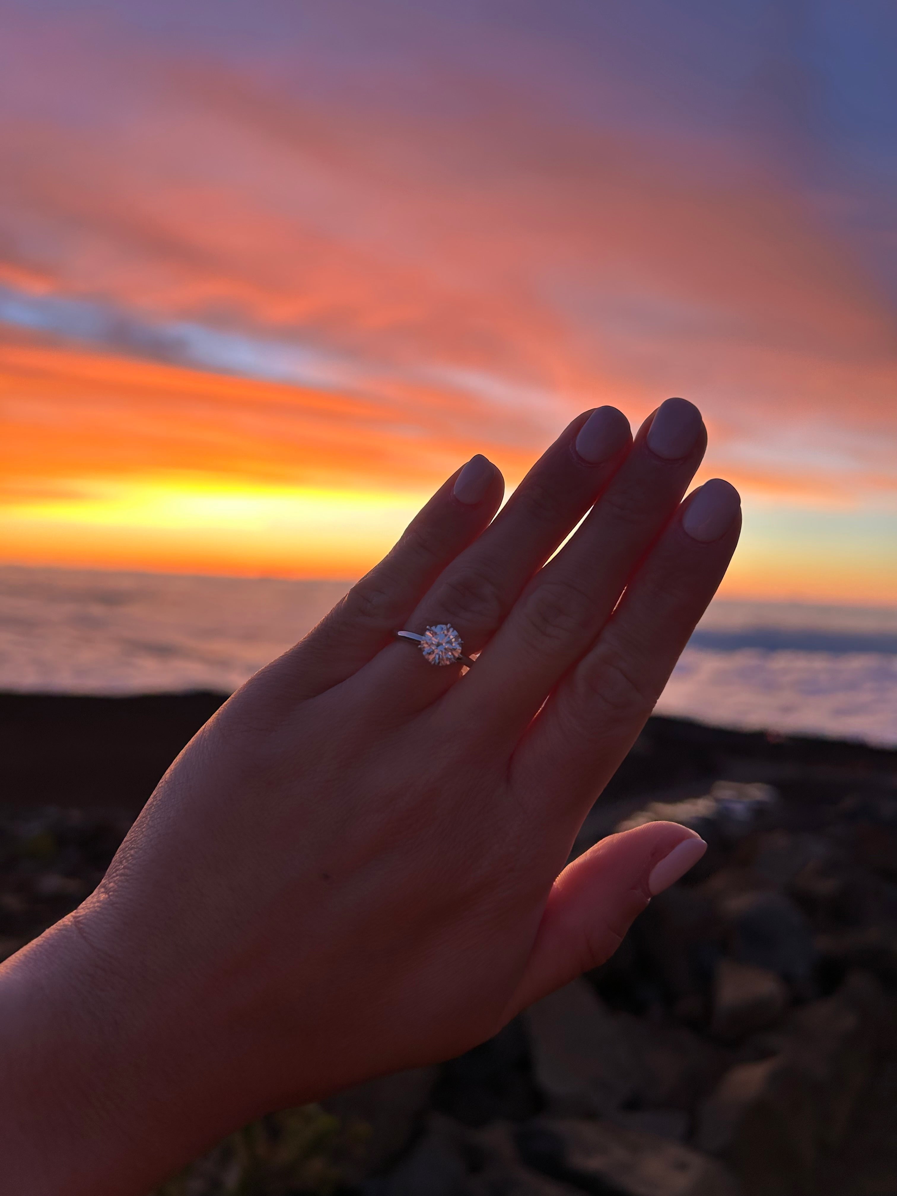 Hand wearing a tinxx ring with a sunset in Hawaii