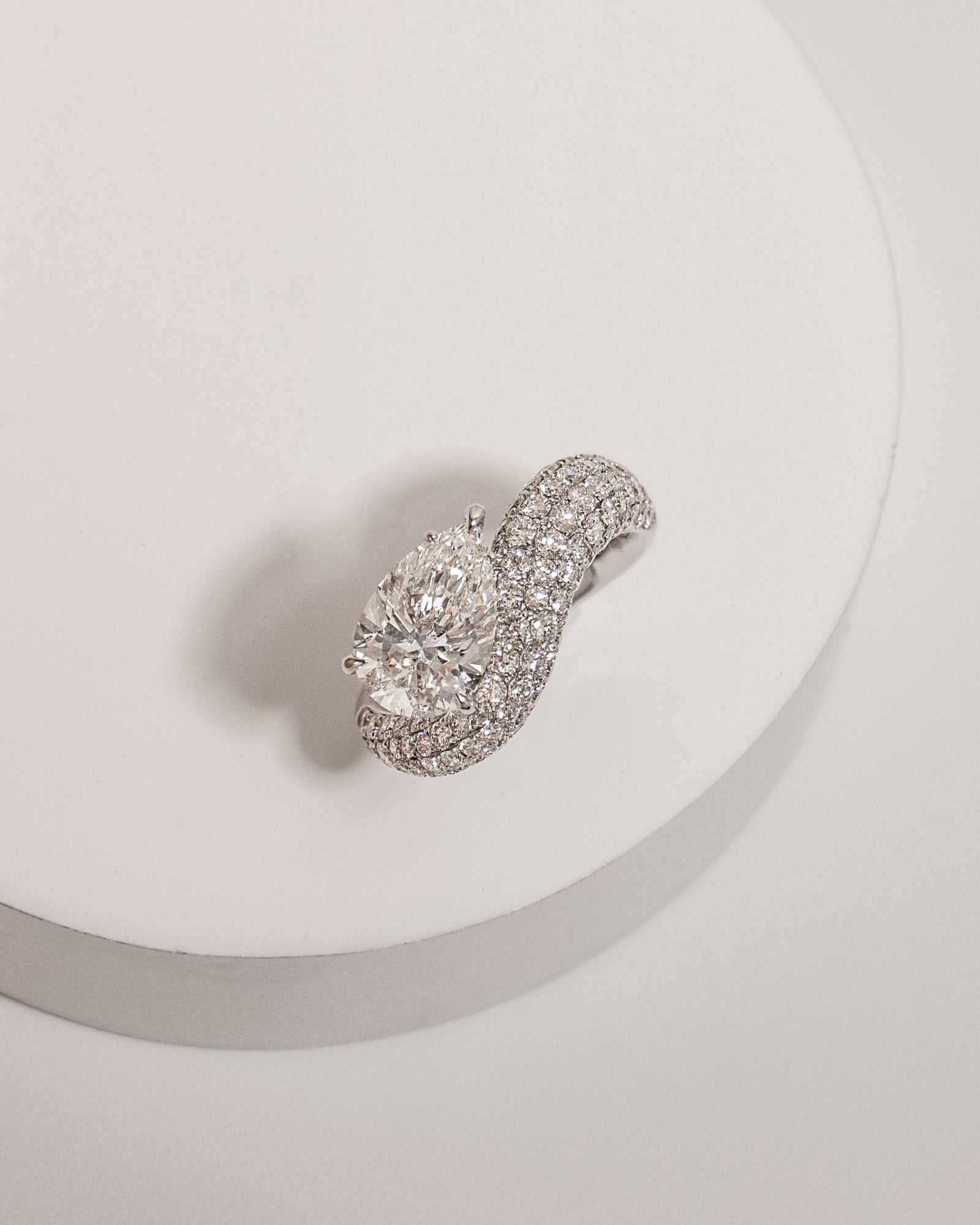 Pear cut diamond wave pavé dome ring in white gold, styled on a sculptural stand