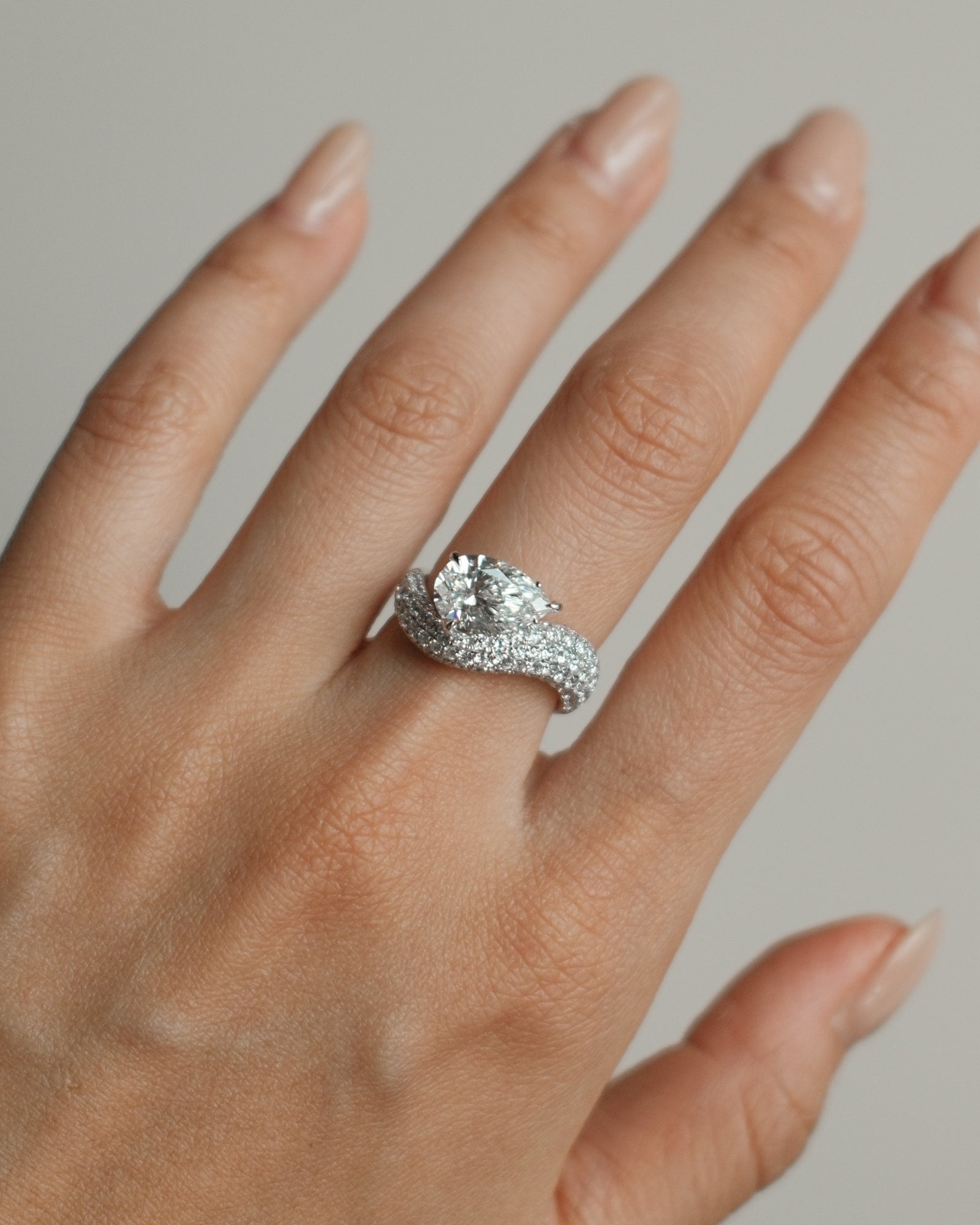 Pear cut diamond wave pavé dome ring in white gold worn on hand