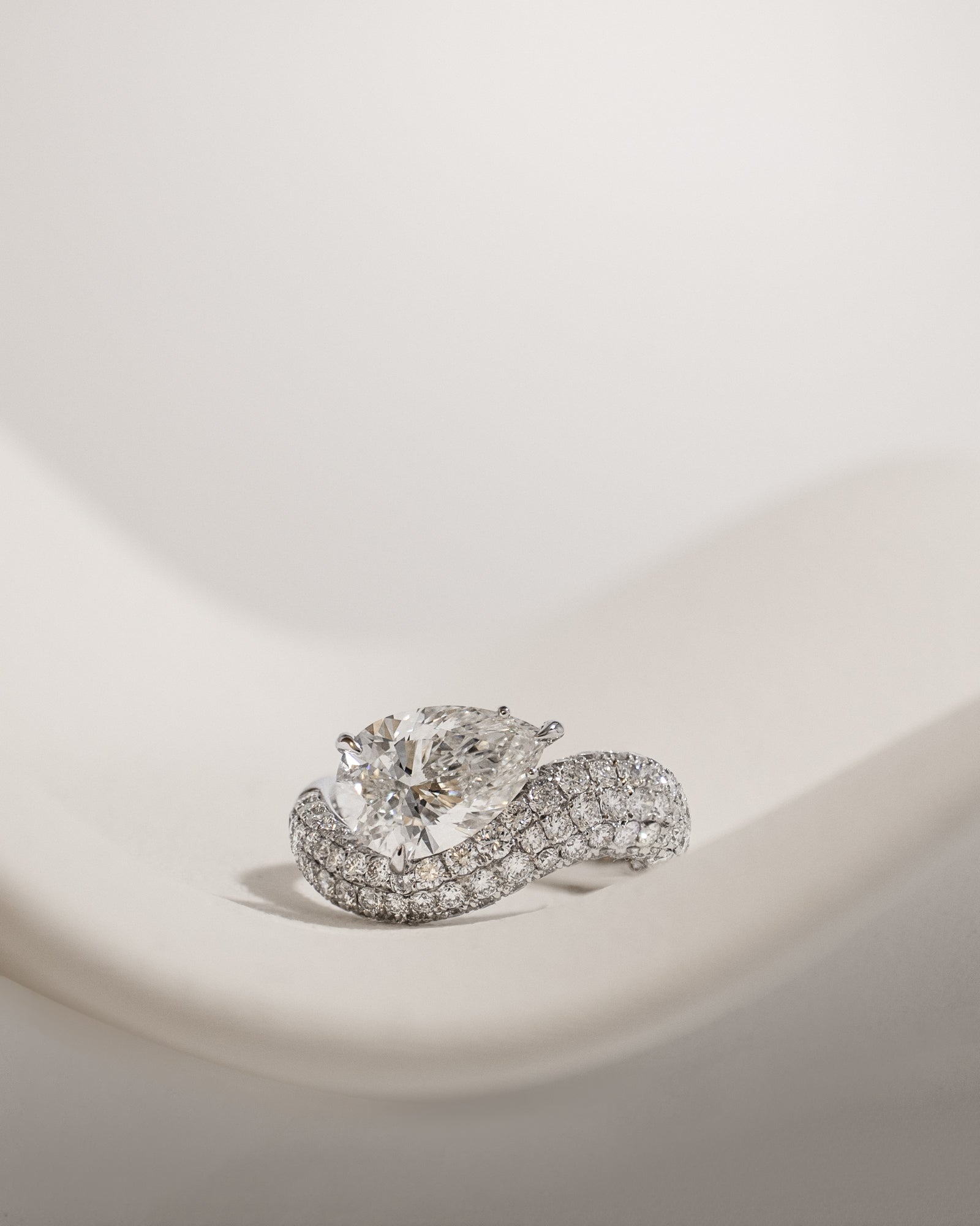 Pear cut diamond wave pavé dome ring in white gold, styled on a sculptural stand
