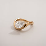 Front view of a pear diamond gold wave ring in 18K yellow gold against a light background