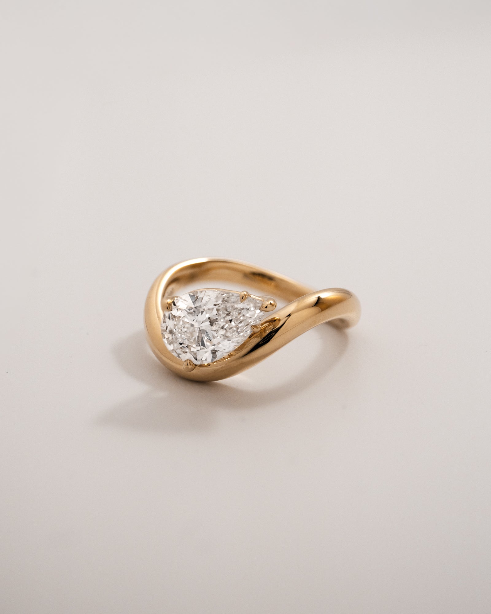 Front view of a pear diamond gold wave ring in 18K yellow gold against a light background