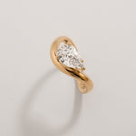 Top view of a pear diamond gold wave ring in 18K yellow gold against a light background
