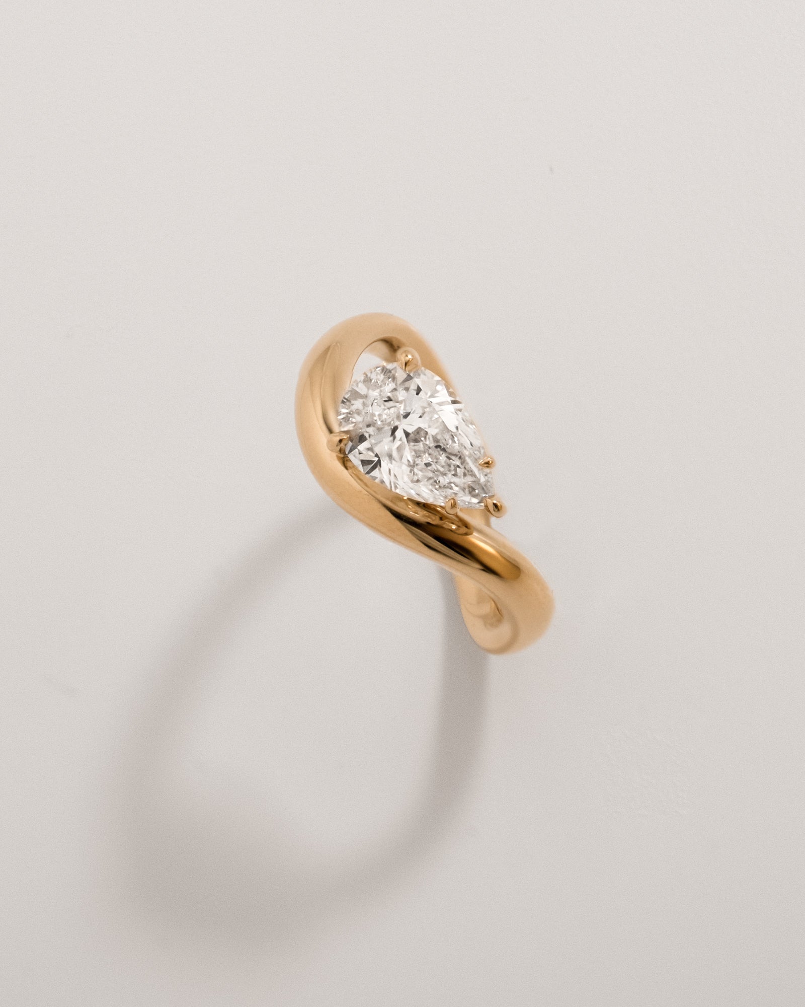Top view of a pear diamond gold wave ring in 18K yellow gold against a light background
