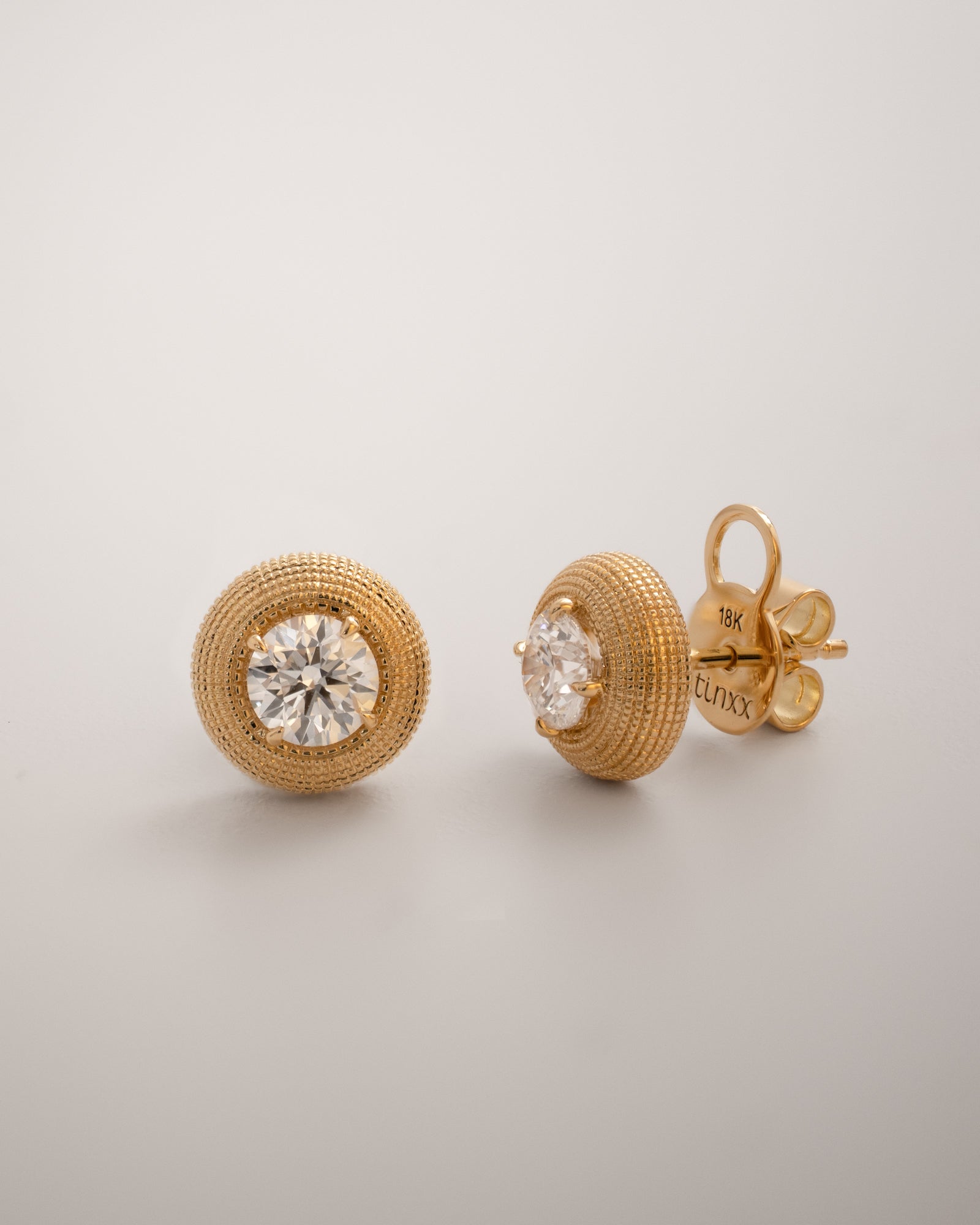 Round cut diamond stud earrings with textured gold surround in yellow gold, showing the earring backing