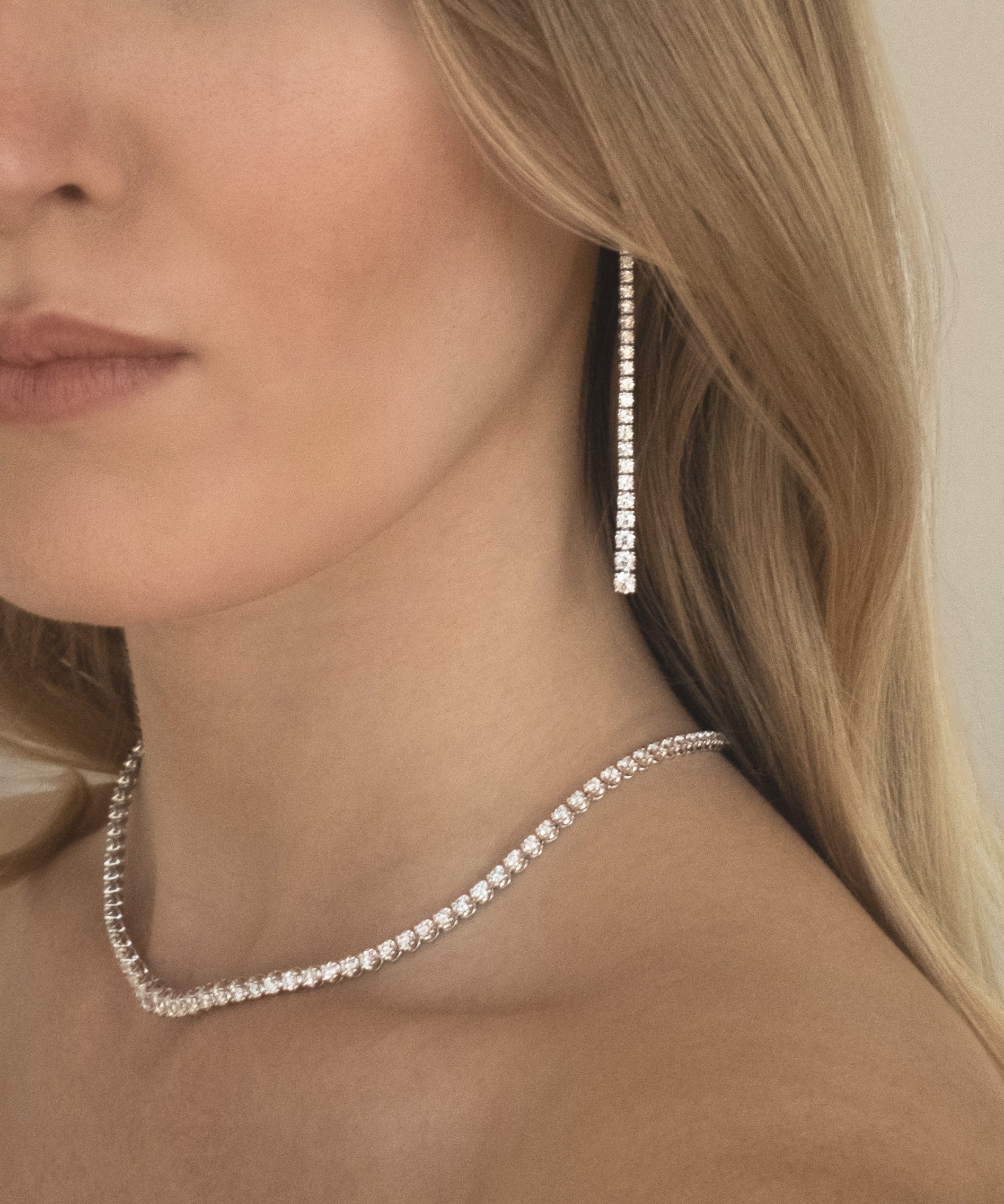 Close-up of a woman wearing a graduated long drop lab grown diamond earrings and tennis necklace in 18K white gold from tinxx.