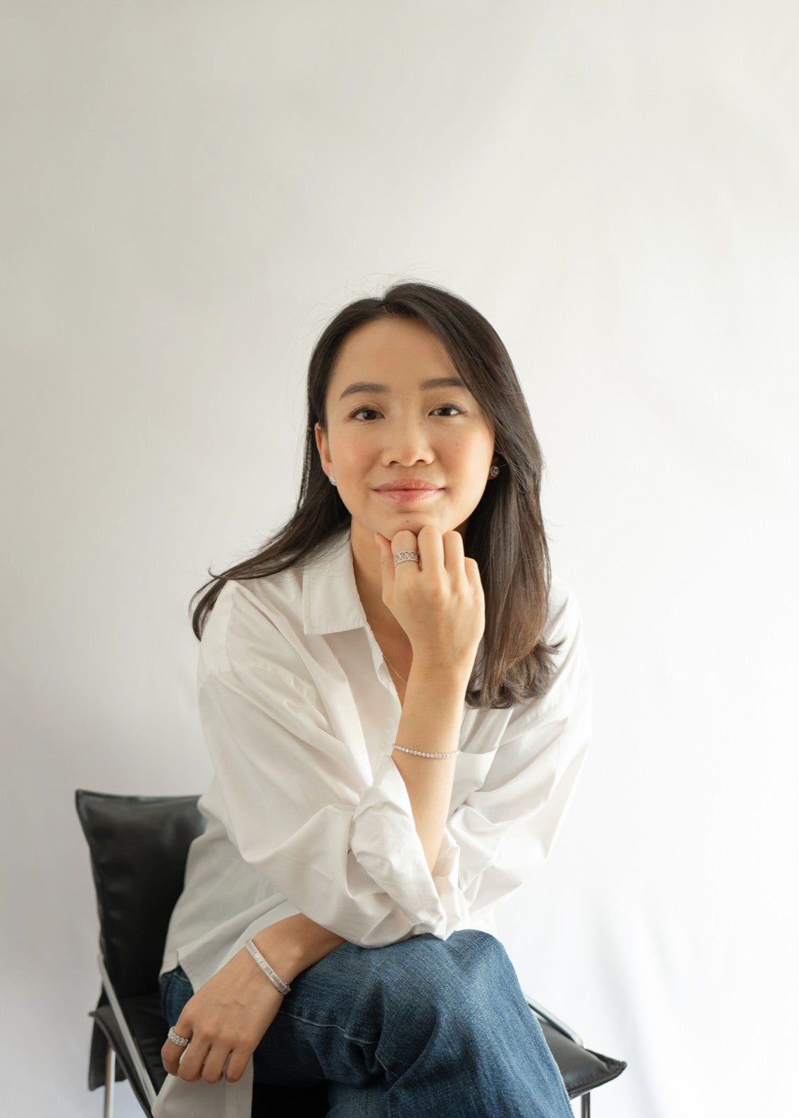 tinxx jewelry founder, evadne, wearing a white shirt and blue jeans sitting on a chair against a plain background