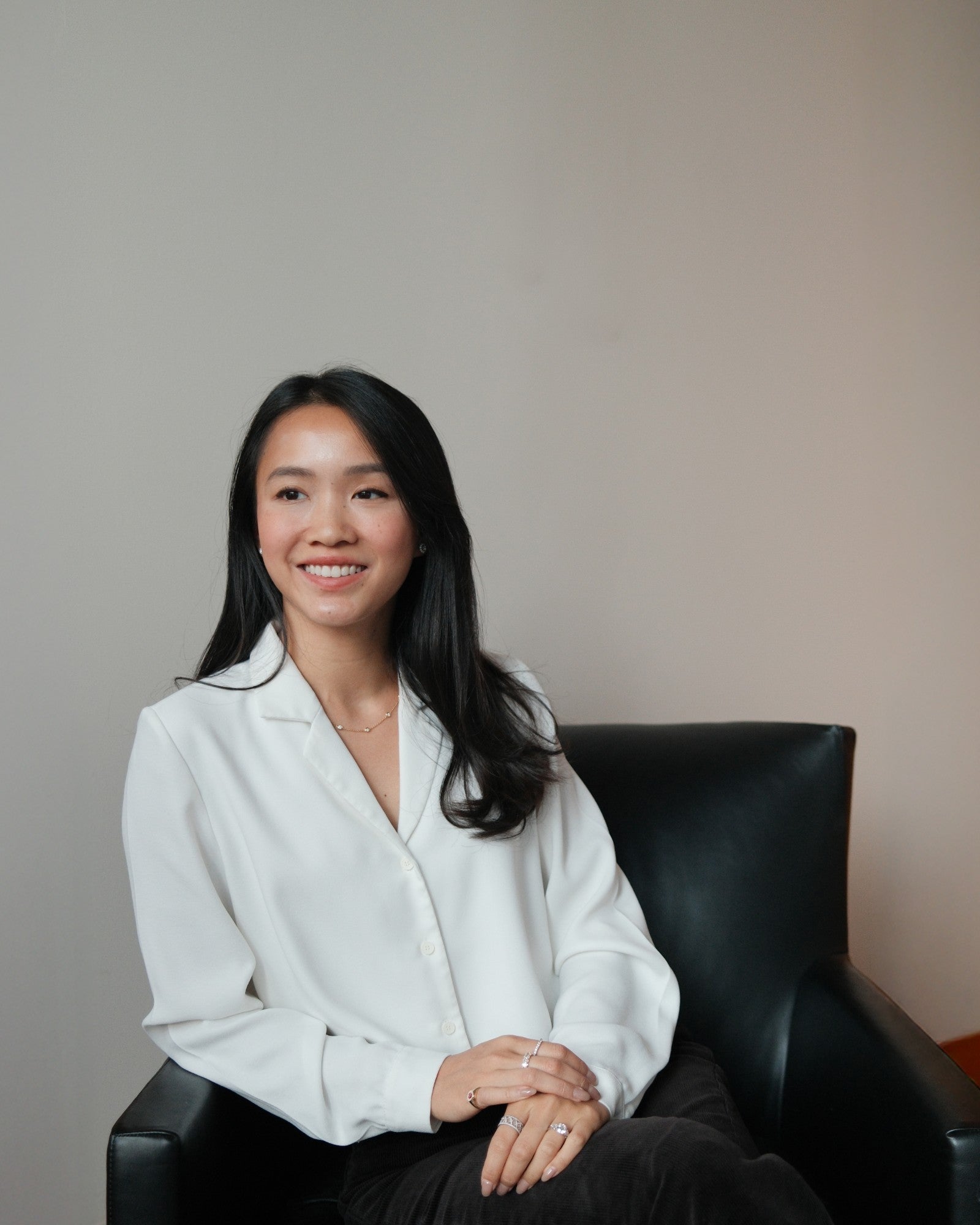 Evadne, tinxx jewelry founder, in a white blouse sitting on a black chair against a plain background