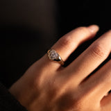 Heart shaped diamond signet ring in 18K gold on a pinky finger with a blurred background
