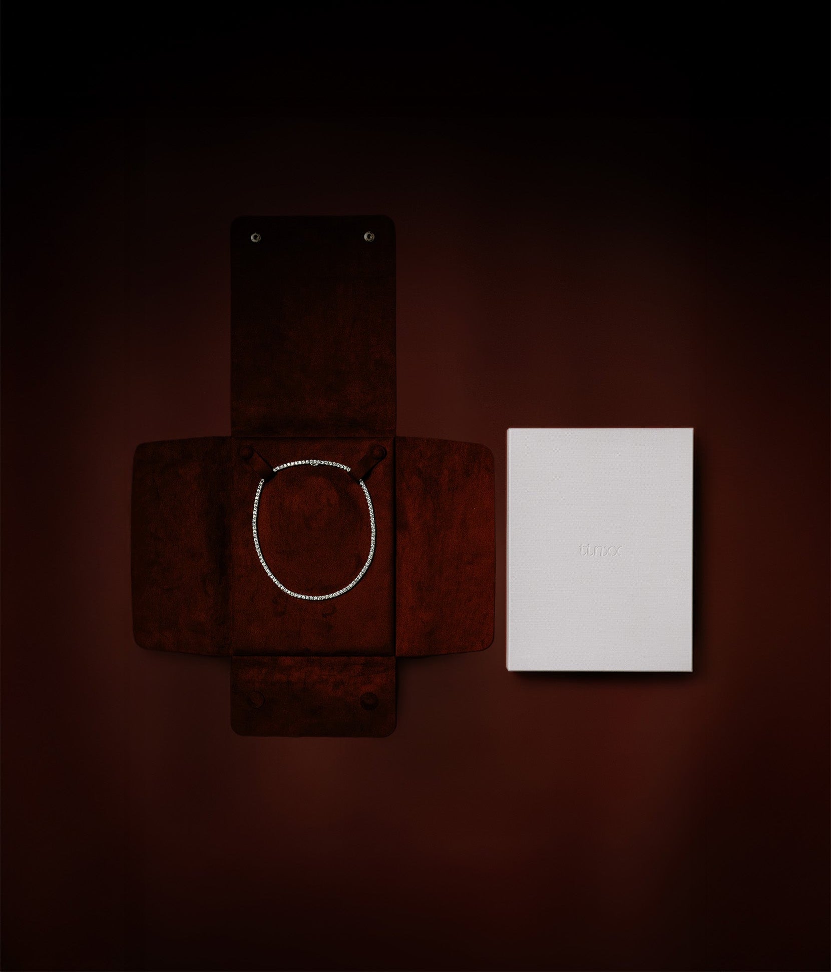 A wine red suede necklace pouch with a white exterior box packaging with tinxx logo debossed