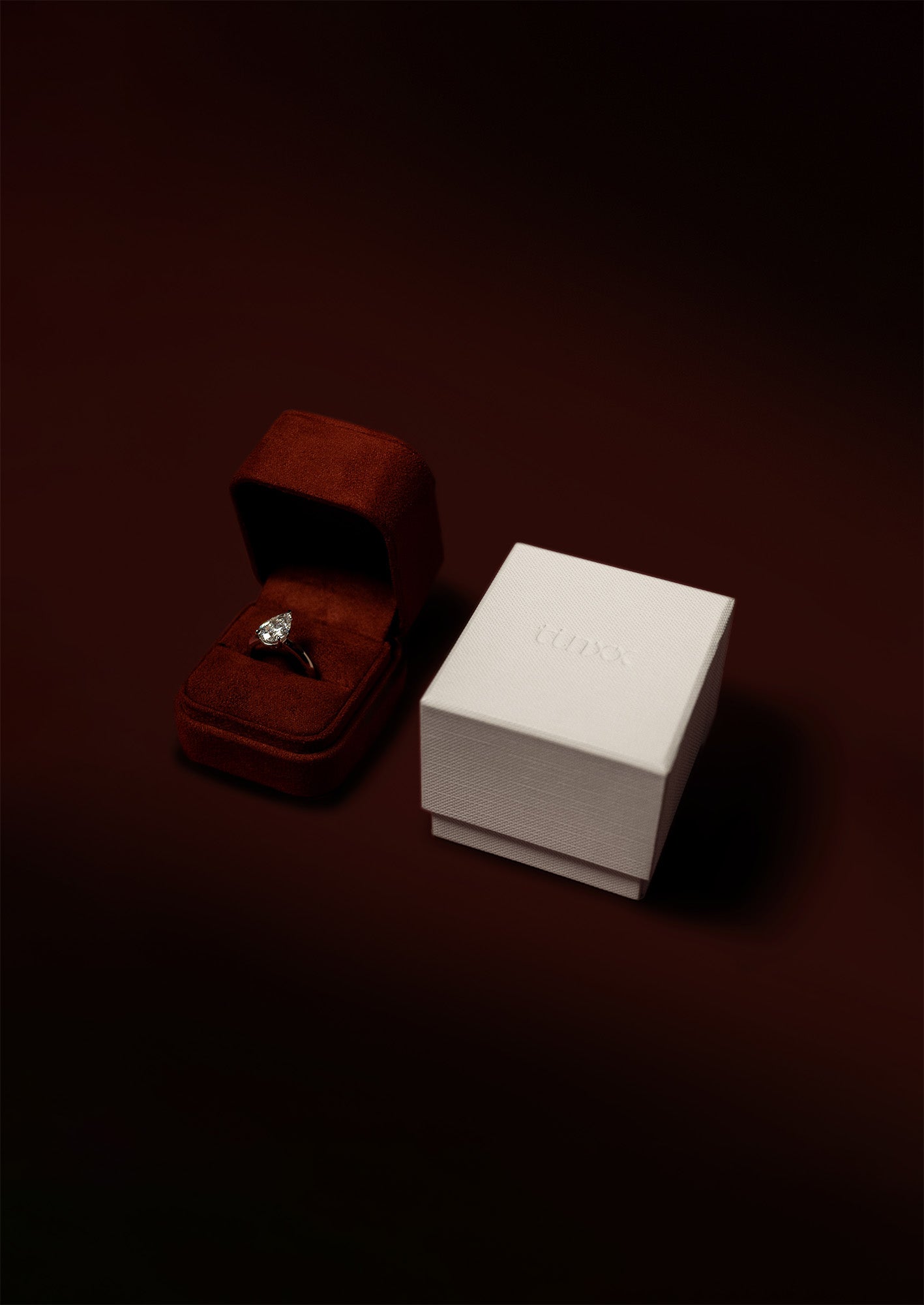 A wine red suede ring box with a white exterior box packaging with tinxx logo debossed