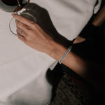 Hand holding a glass of red wine with a white tablecloth in the background, wearing a tinxx lab grown bangle