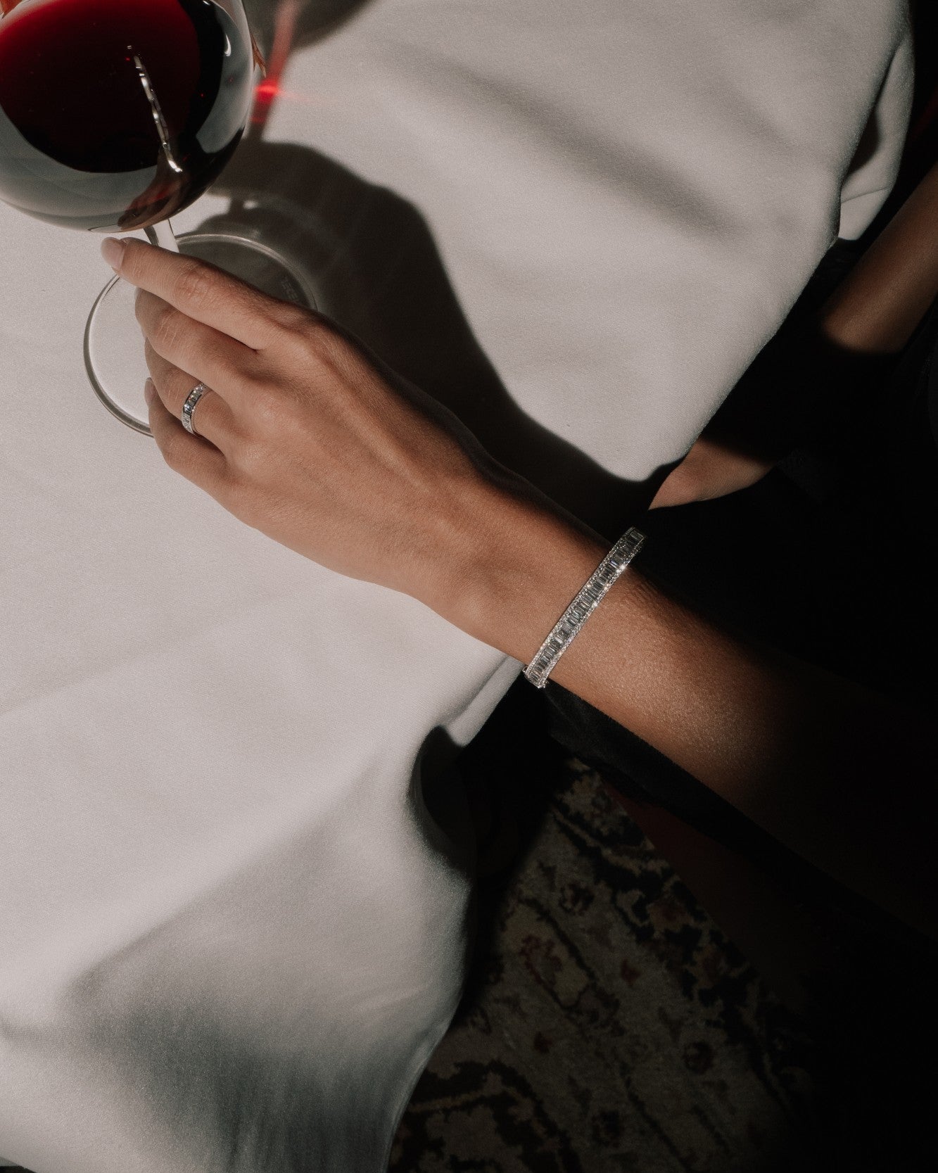Hand holding a glass of red wine with a white tablecloth in the background, wearing a tinxx lab grown bangle