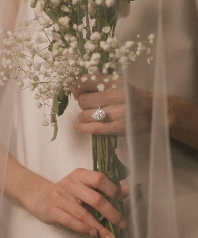 Bride holding a bouquet of flowers with a pear cut lab grown diamond halo engagement ring from tinxx