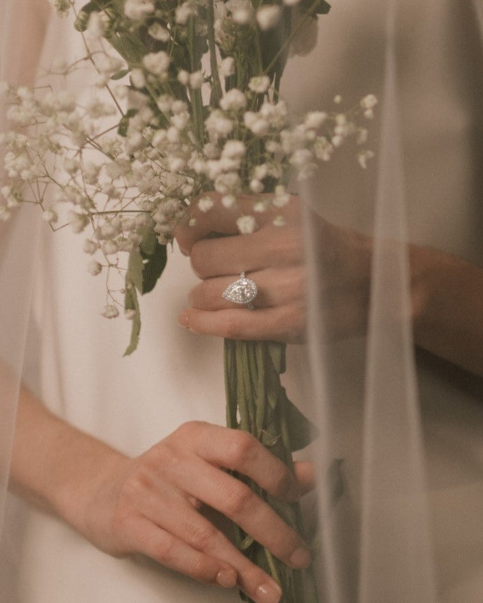 Bride holding a bouquet of flowers with a pear cut lab grown diamond halo engagement ring from tinxx