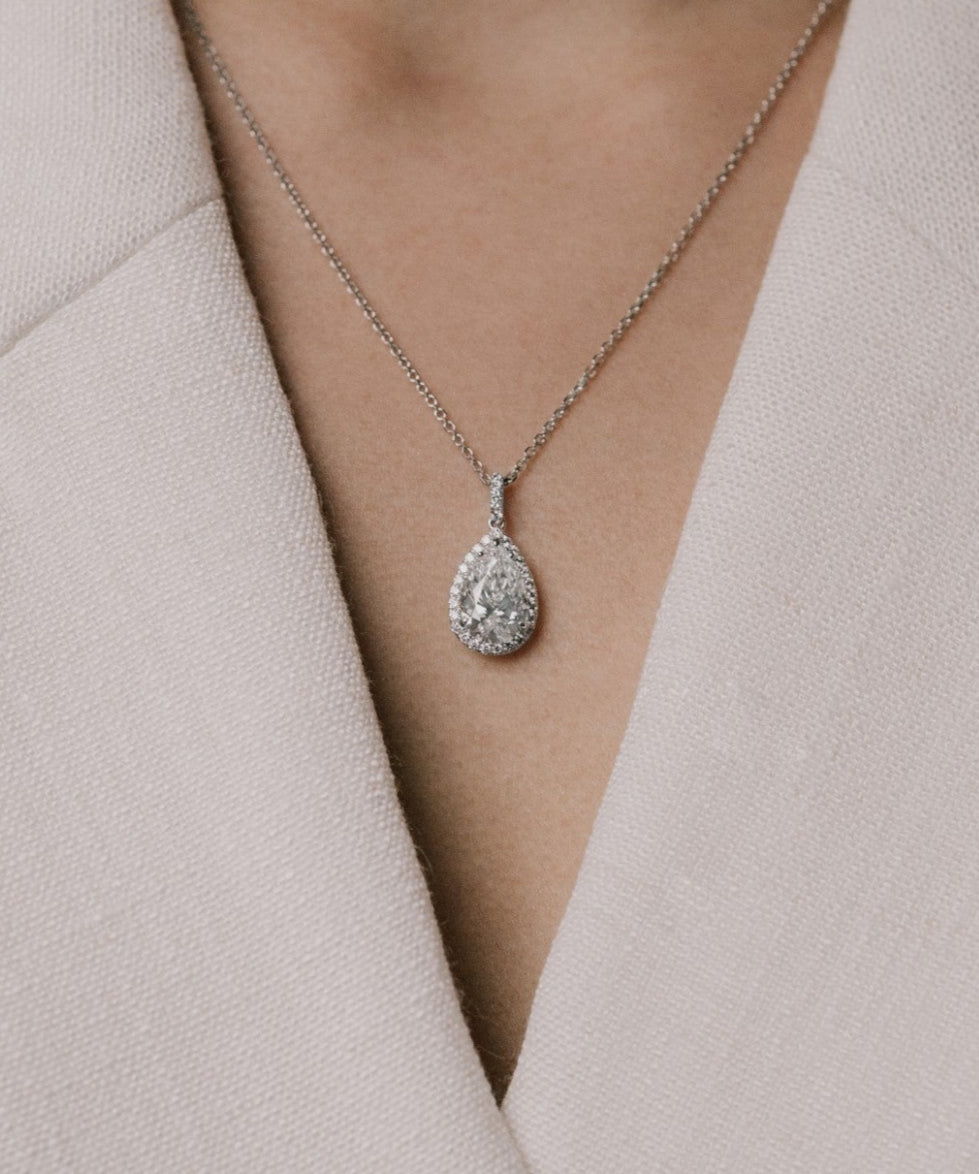 Pear cut lab grown diamond pendant on a delicate chain from tinxx worn by a person in a light-colored outfit.