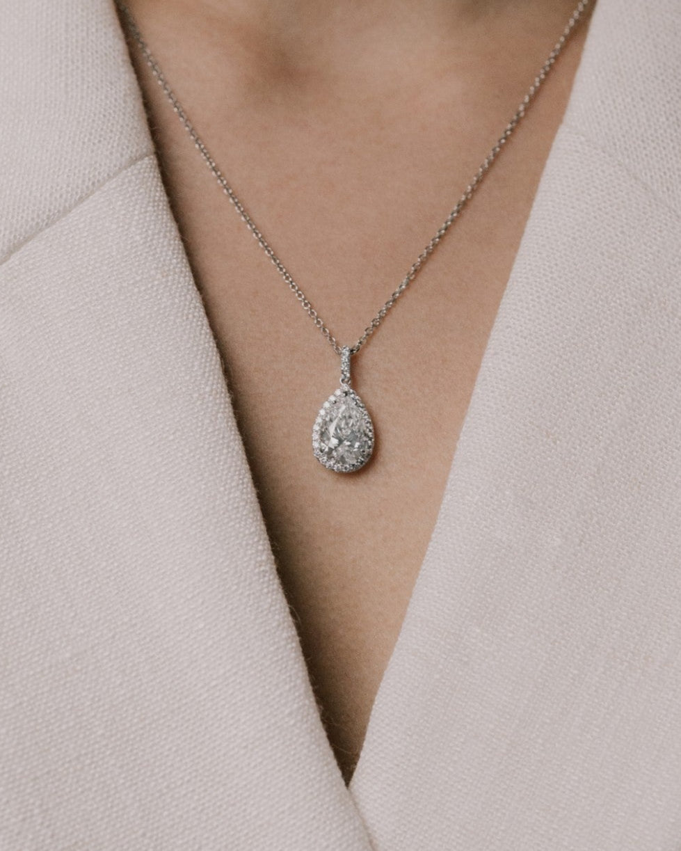 Pear cut lab grown diamond pendant on a delicate chain from tinxx worn by a person in a light-colored outfit.