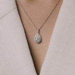 Pear cut lab grown diamond pendant on a delicate chain from tinxx worn by a person in a light-colored outfit.