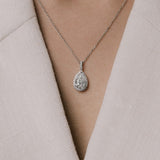 Pear cut lab grown diamond pendant on a delicate chain from tinxx worn by a person in a light-colored outfit.
