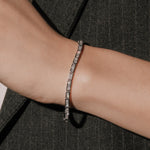 Princess cut lab grown diamond bracelet in a channel setting from tinxx, worn on wrist with a dark tailored jacket, photographed in flash.