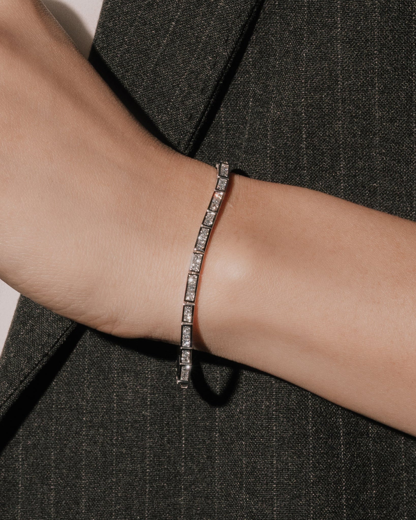 Princess cut lab grown diamond bracelet in a channel setting from tinxx, worn on wrist with a dark tailored jacket, photographed in flash.