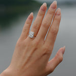 Hand wearing a tinxx lab grown radiant cut diamond halo ring with a blurred natural background