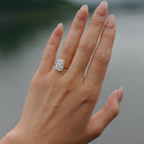 Hand wearing a tinxx lab grown radiant cut diamond halo ring with a blurred natural background