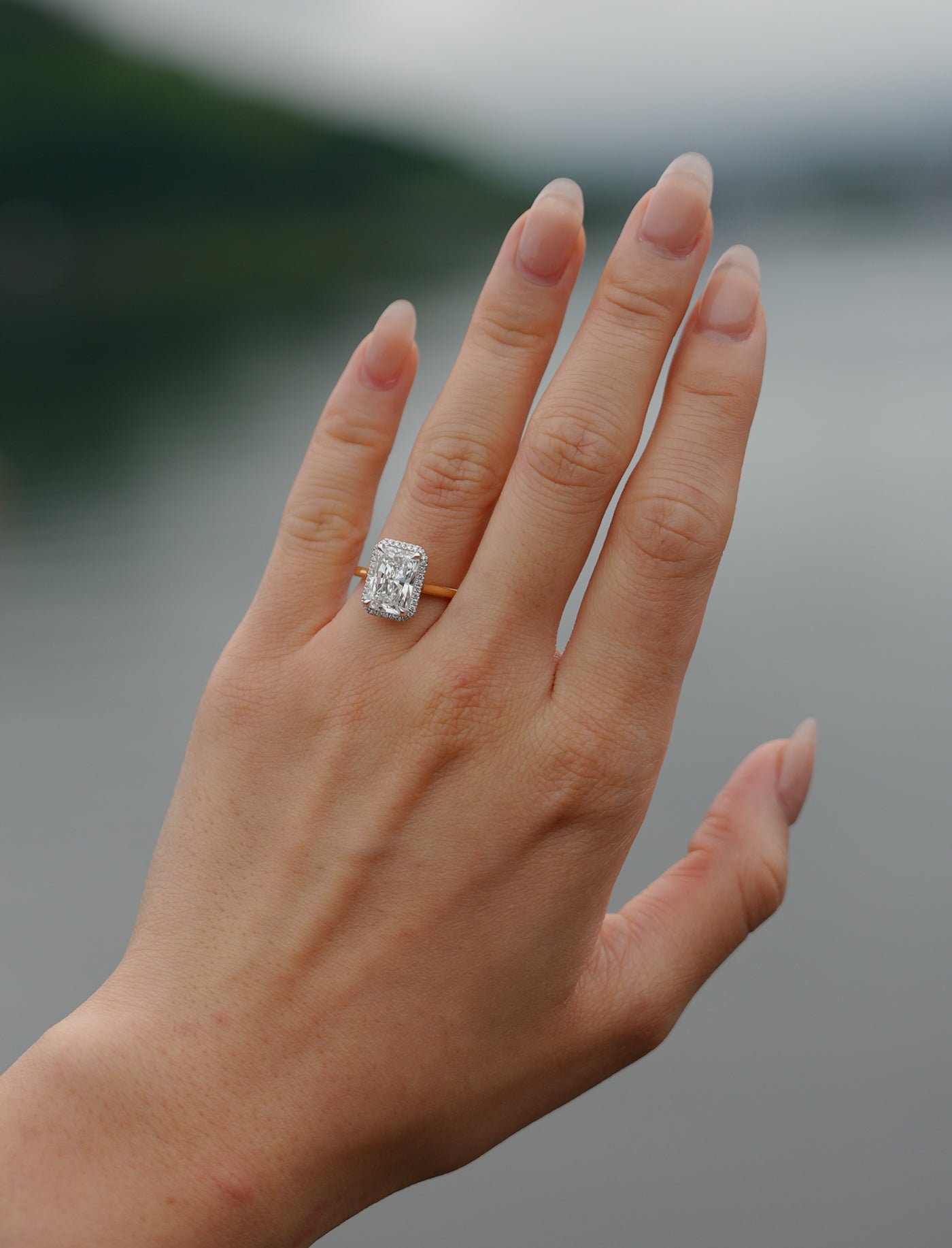 Hand wearing a tinxx lab grown radiant cut diamond halo ring with a blurred natural background