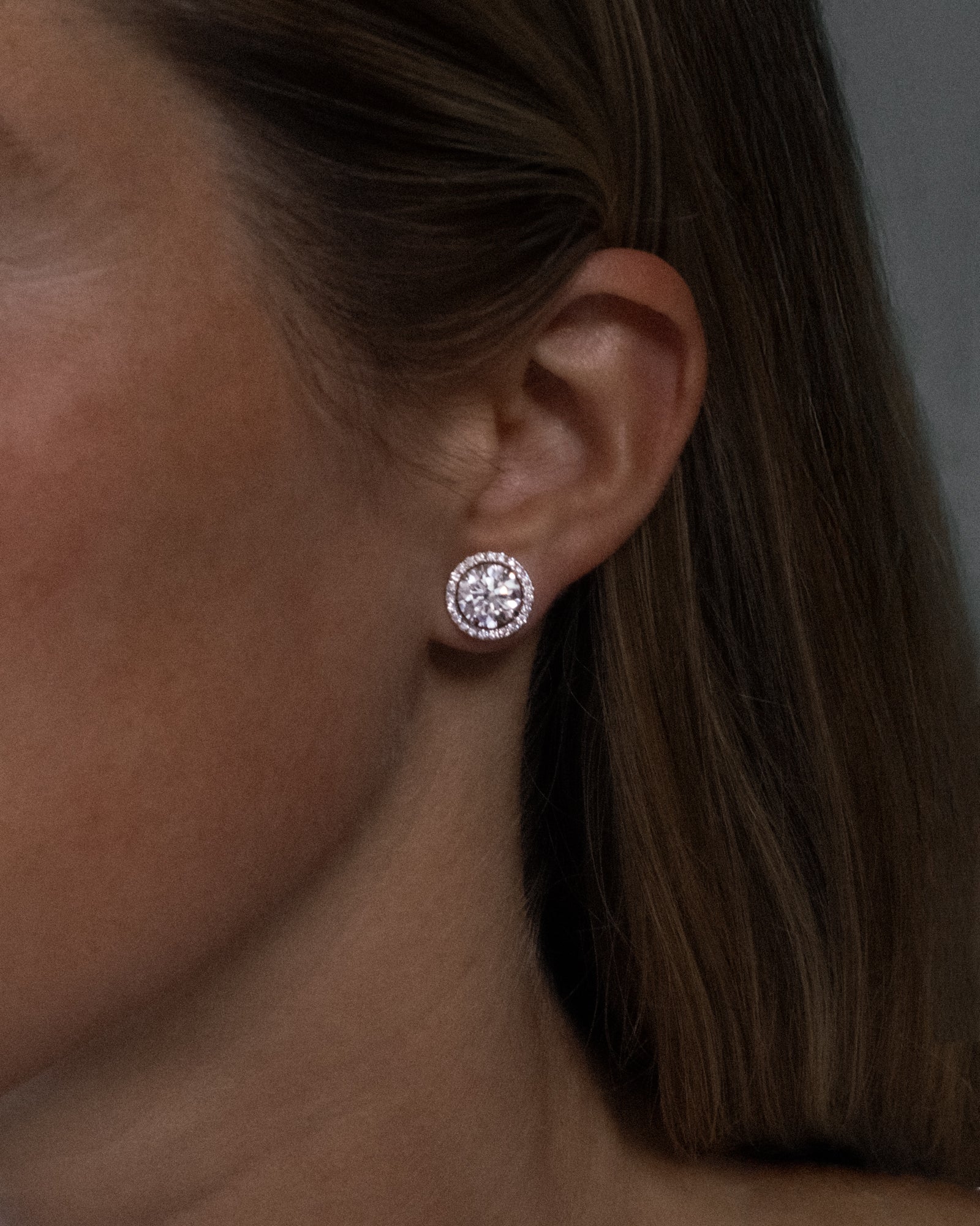 Round cut lab grown diamond stud earrings with removable halo in 18K white gold from tinxx, shown worn on ear.