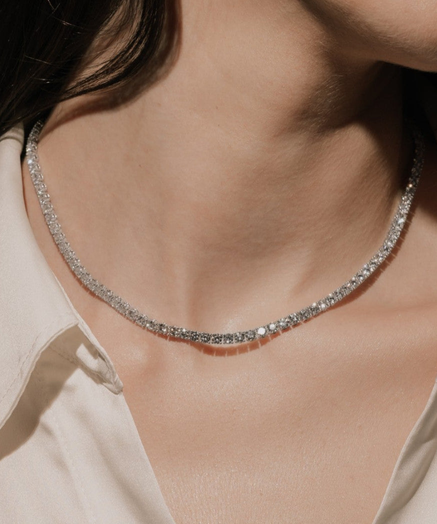 Round cut lab grown diamond tennis necklace in a four-prong setting from tinxx, worn by a woman, photographed in flash photography.