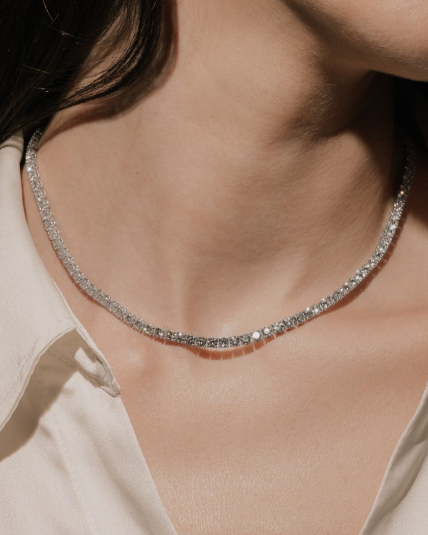 Round cut lab grown diamond tennis necklace in a four-prong setting from tinxx, worn by a woman, photographed in flash photography.