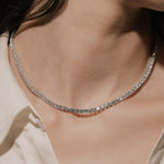 Round cut lab grown diamond tennis necklace in a four-prong setting from tinxx, worn by a woman, photographed in flash photography.