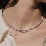 Round cut lab grown diamond tennis necklace in a four-prong setting from tinxx, worn by a woman, photographed in flash photography.